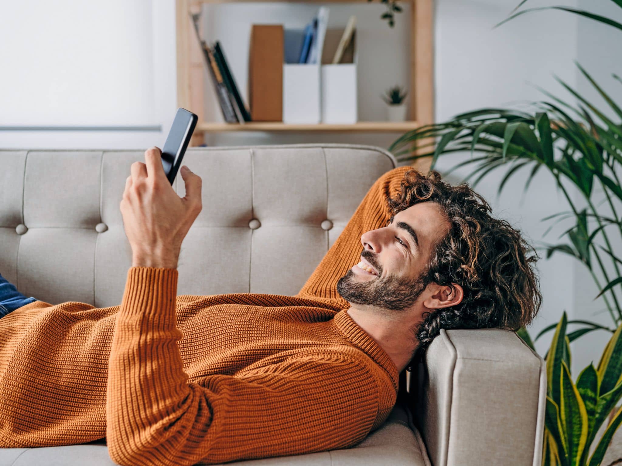 Newsletter bestellen: Lächelnder Mann liegt auf Couch und hält Smartphone in der Hand
