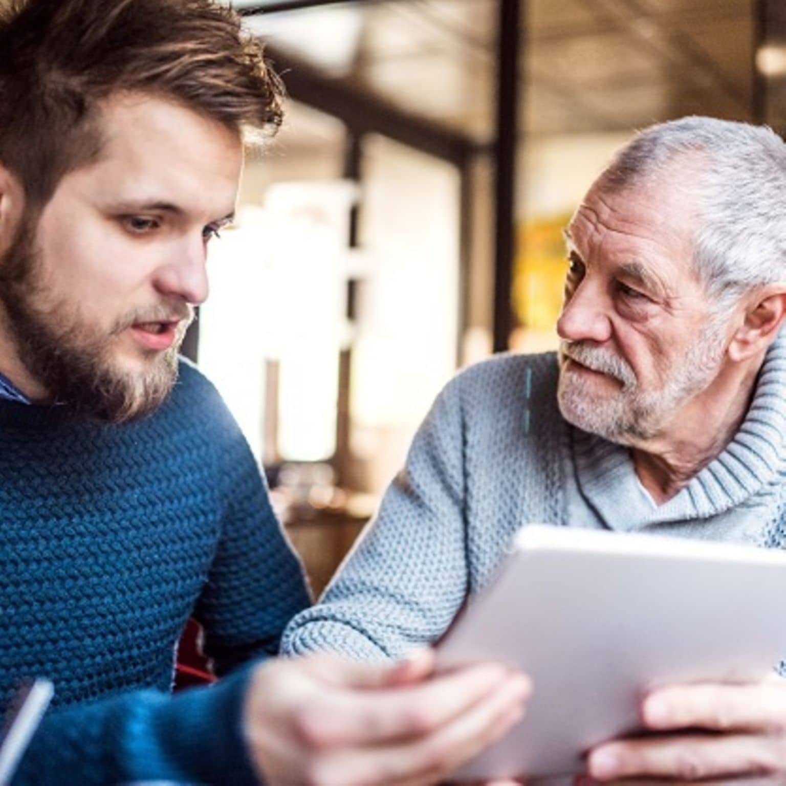 Recht auf Zweitmeinung: Jüngerer Mann im Gespräch mit älterem Mann. Sie halten einen Stapel Papier vor sich.
