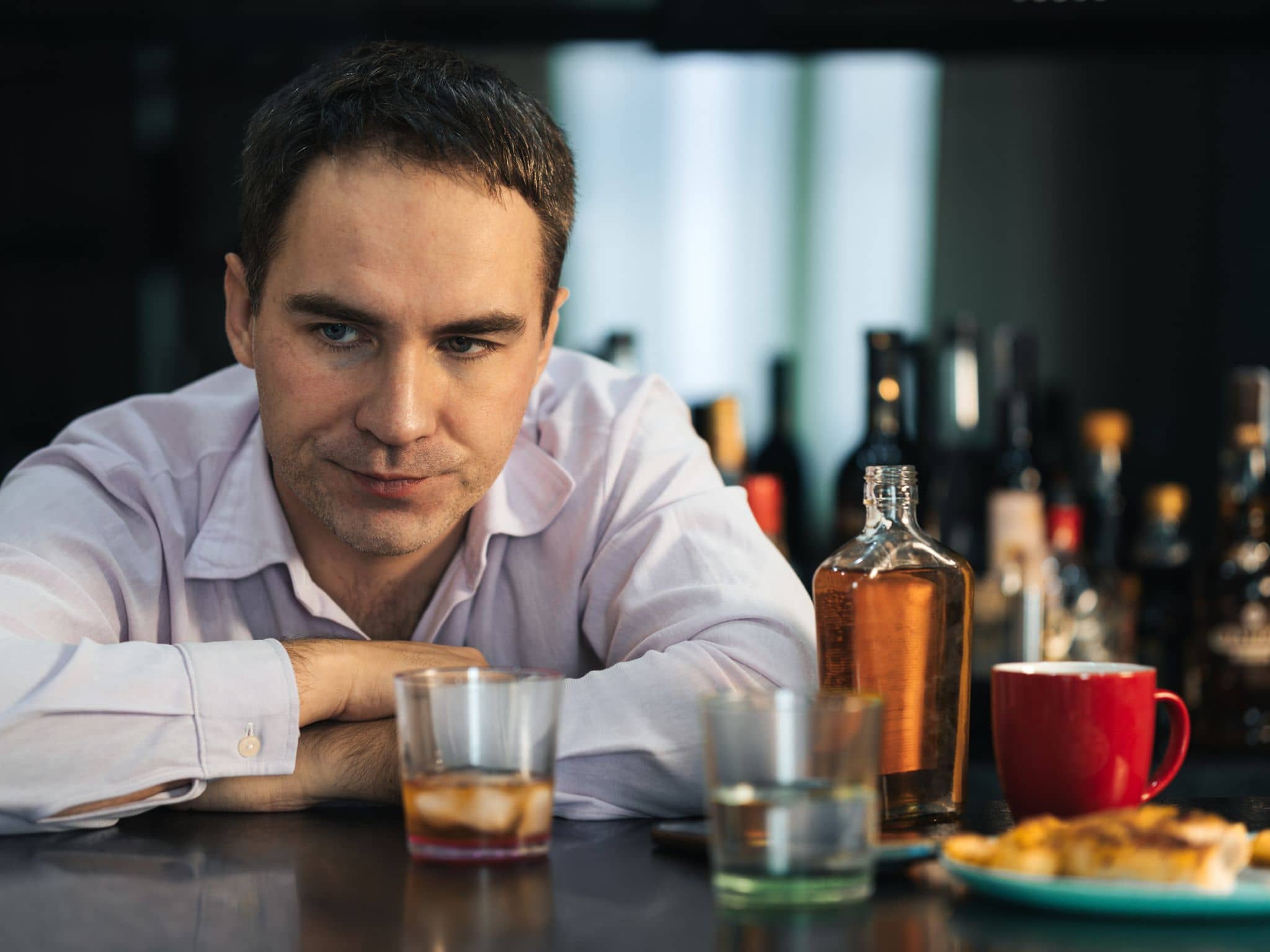 Ein junger Geschäftsmann sitzt an einem Tresen, auf dem viele leere Gläser stehen
