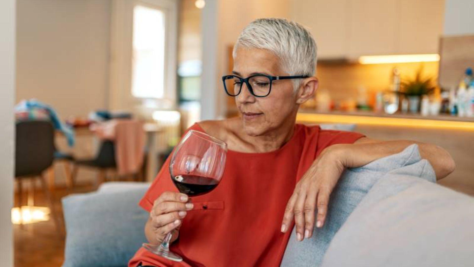 Sucht: Ältere Frau sitzt auf der Couch und blickt in ein volles Weinglas
