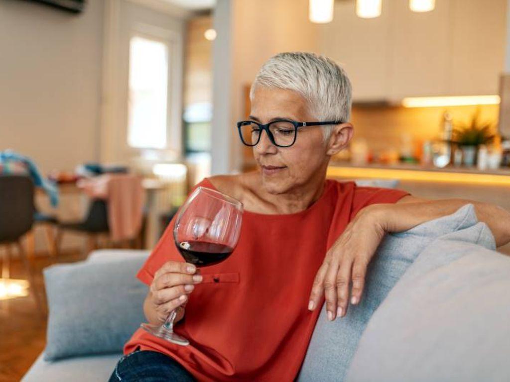 Sucht: Ältere Frau sitzt auf der Couch und blickt in ein volles Weinglas