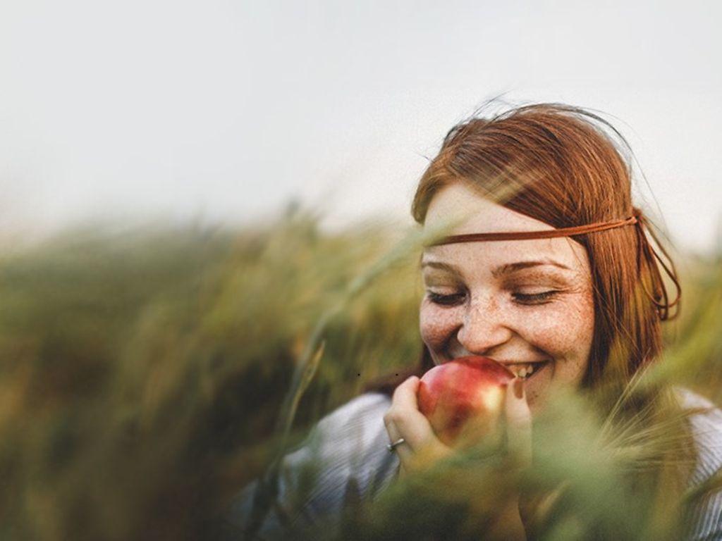 Bild: Naturverbundene Frau in einem Weizenfeld beißt in einen Apfel.
