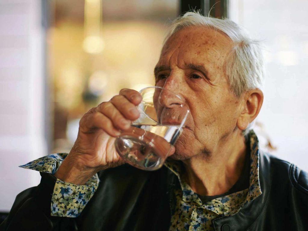 Prostatabeschwerden: Älterer Mann trinkt ein Glas Wasser.