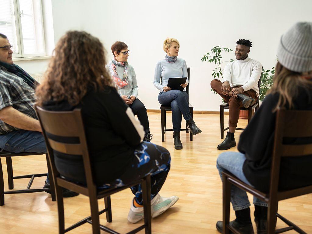 Bild: Personen sitzen in einem Stuhlkreis zur Gruppentherapie.