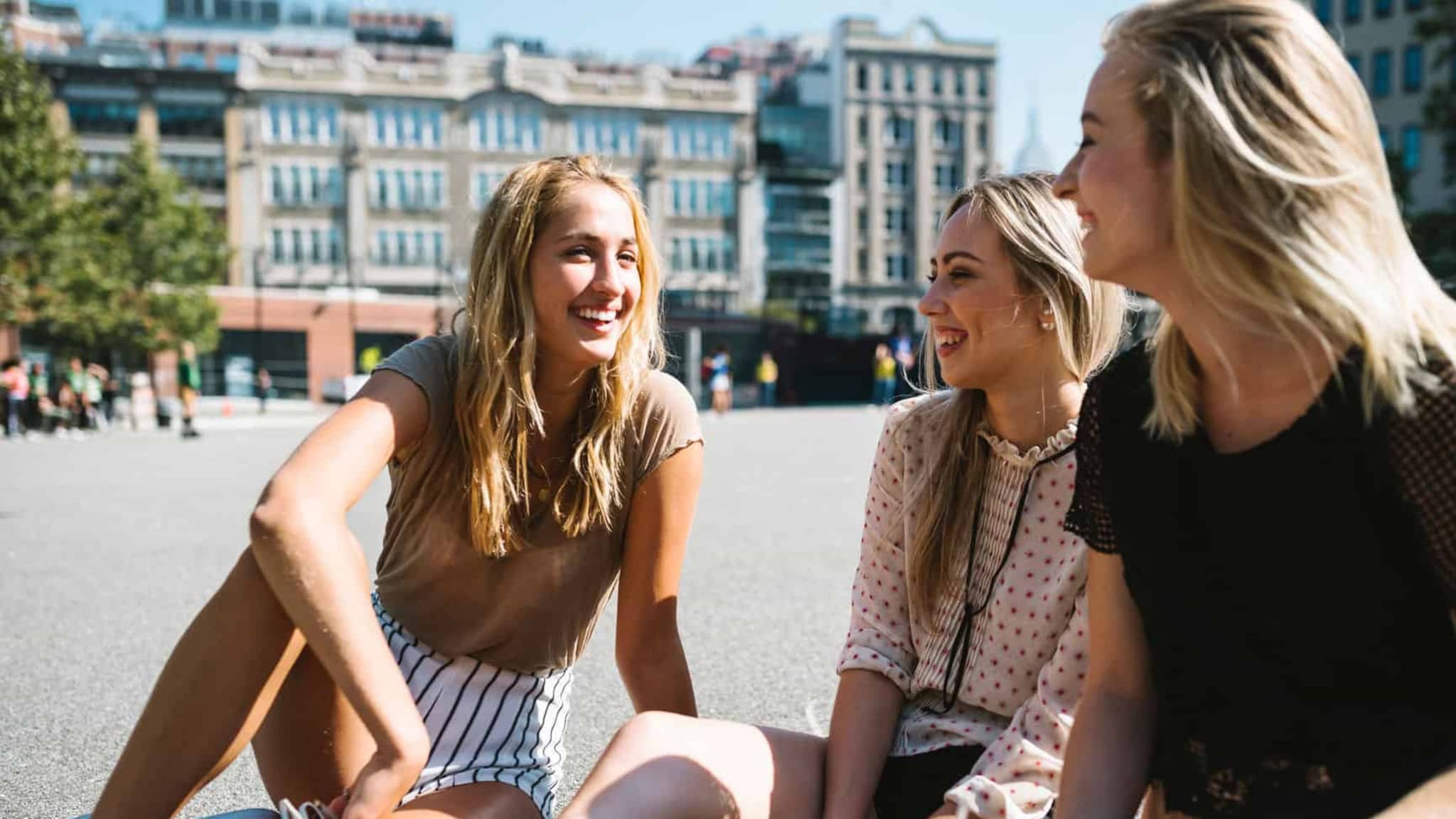 Präventionskampagnen: Drei Teenagerinnen sitzen auf einem Platz auf dem Boden und unterhalten sich.