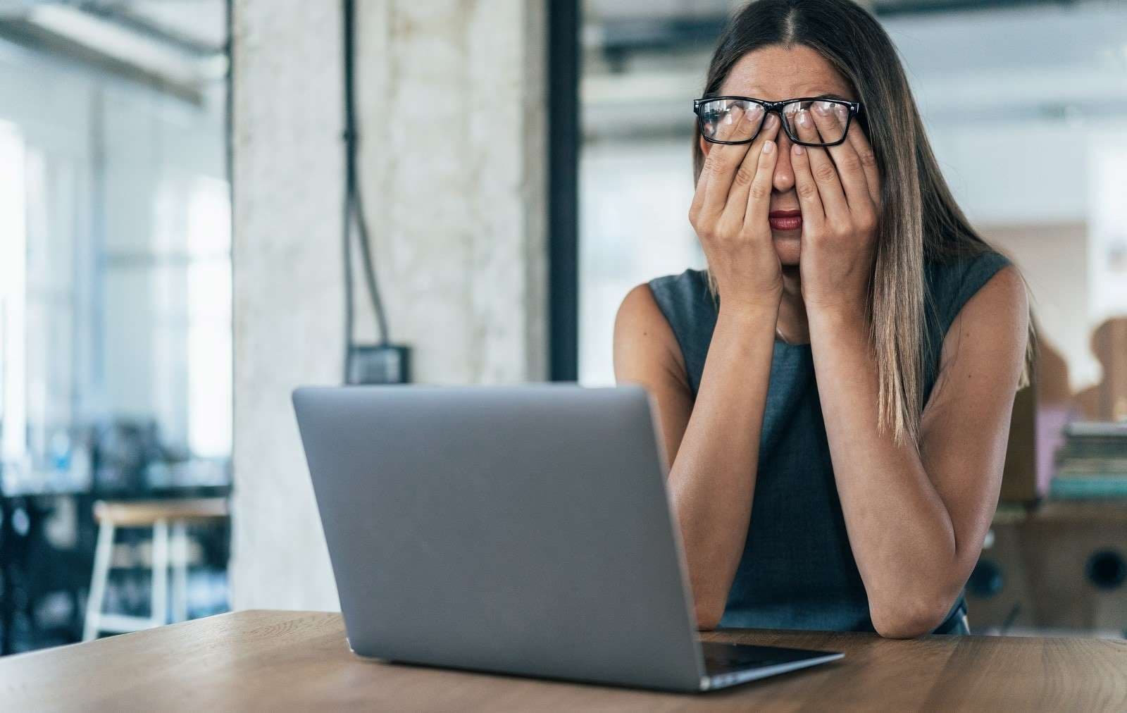 Psychreport: Erschöpft wirkende Frau sitzt vor einem Notebook und reibt sich die Augen.