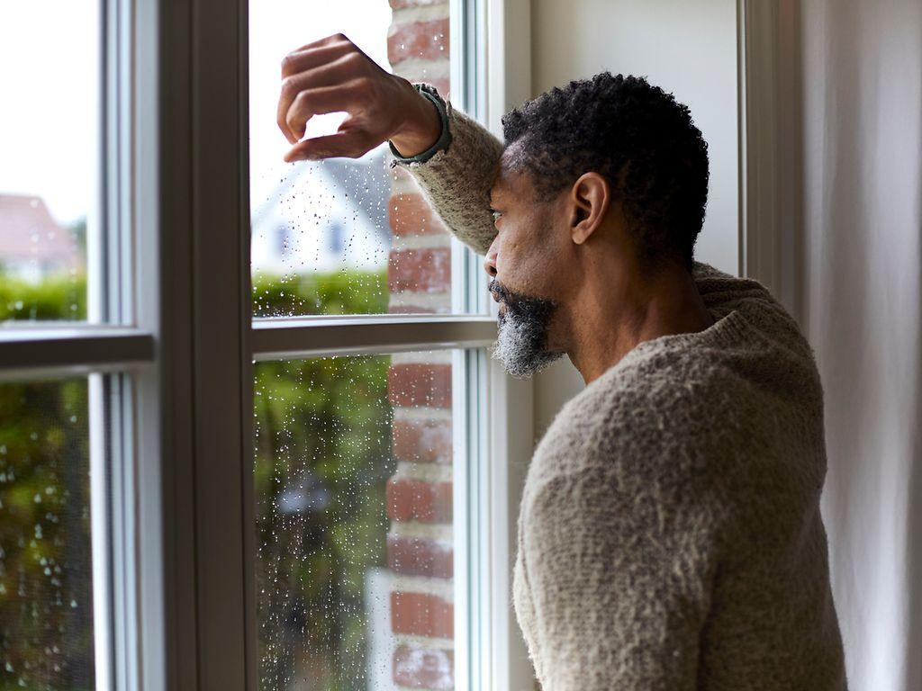 Bild: Trauriger Mann schaut bei Regenwetter aus dem Fenster.