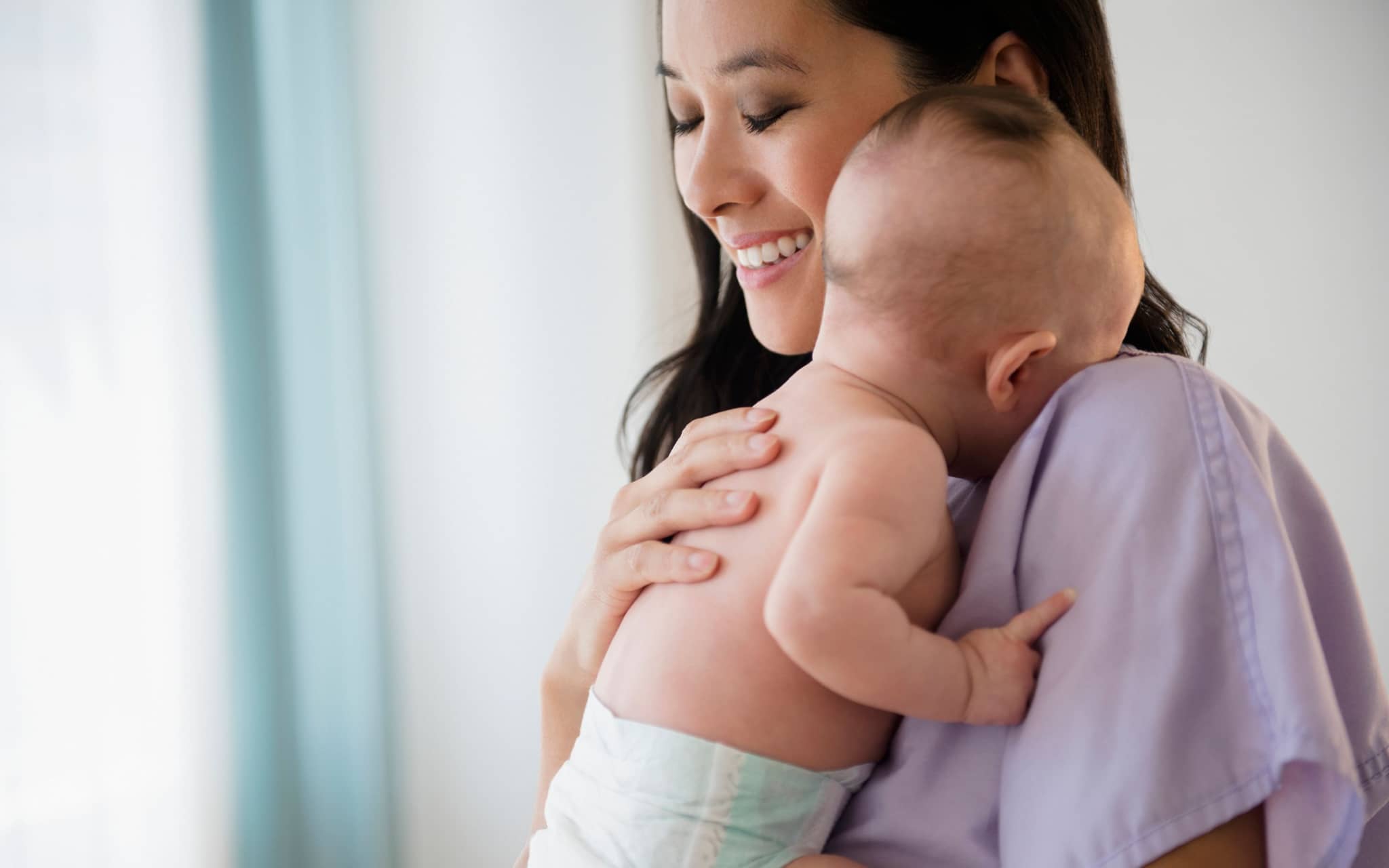 Bild: Asiatische Frau hält ein Baby auf dem Arm und sieht zufrieden aus.