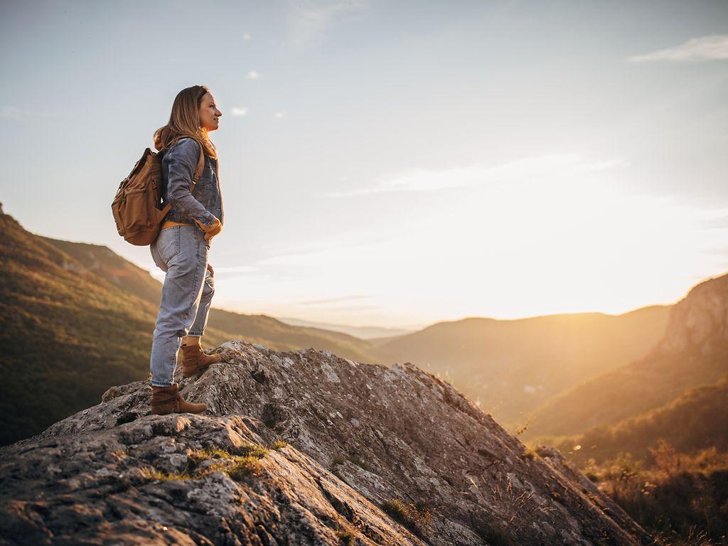Bild: Junge Frau mit Rucksack steht auf einem Bergipfel und betrachtet das malerische Bergpanorama.