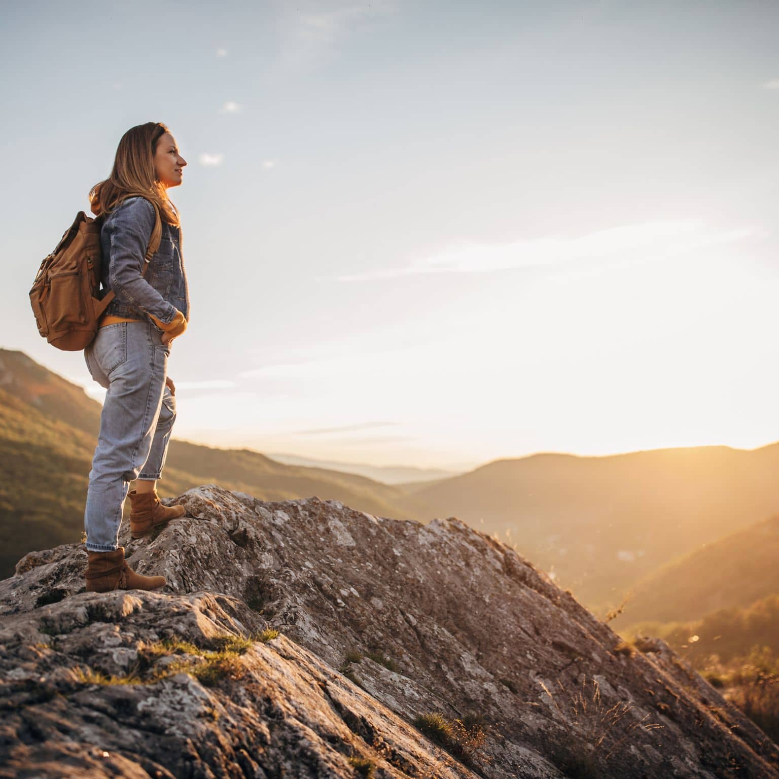Bild: Junge Frau mit Rucksack steht auf einem Bergipfel und betrachtet das malerische Bergpanorama.