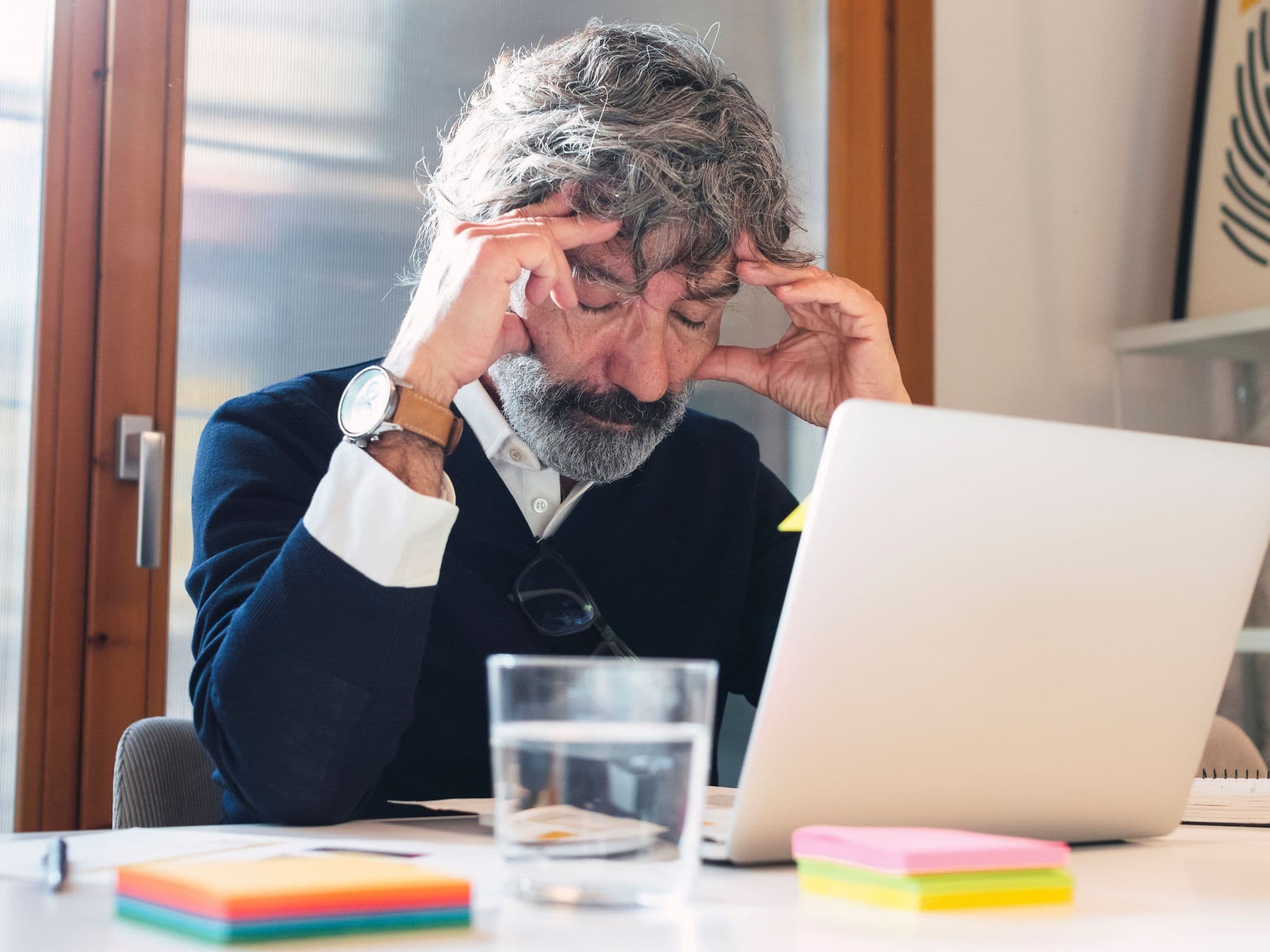 Bild: Älterer Mann sitzt vor einem Laptop und hat die Hände an seinen Schläfen.