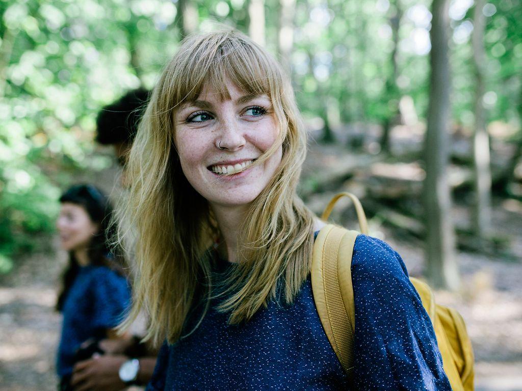 Bild: Junge Frau mit Rucksack freut sich über einen Ausflug in den Wald.