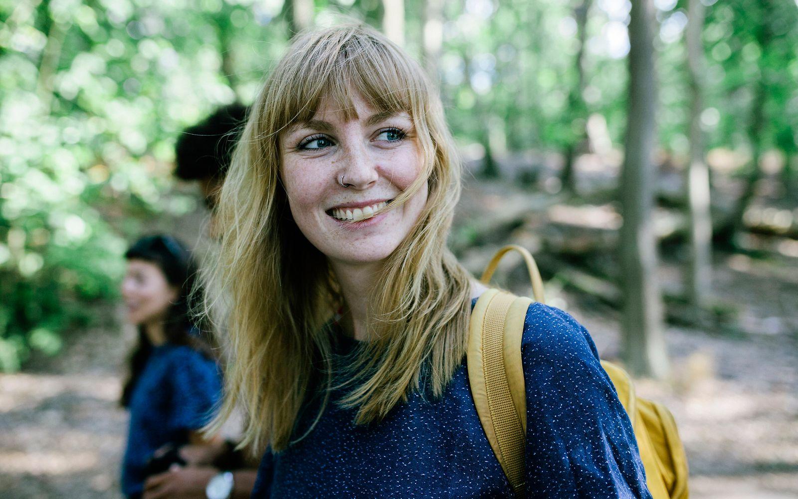 Bild: Junge Frau mit Rucksack freut sich über einen Ausflug in den Wald.