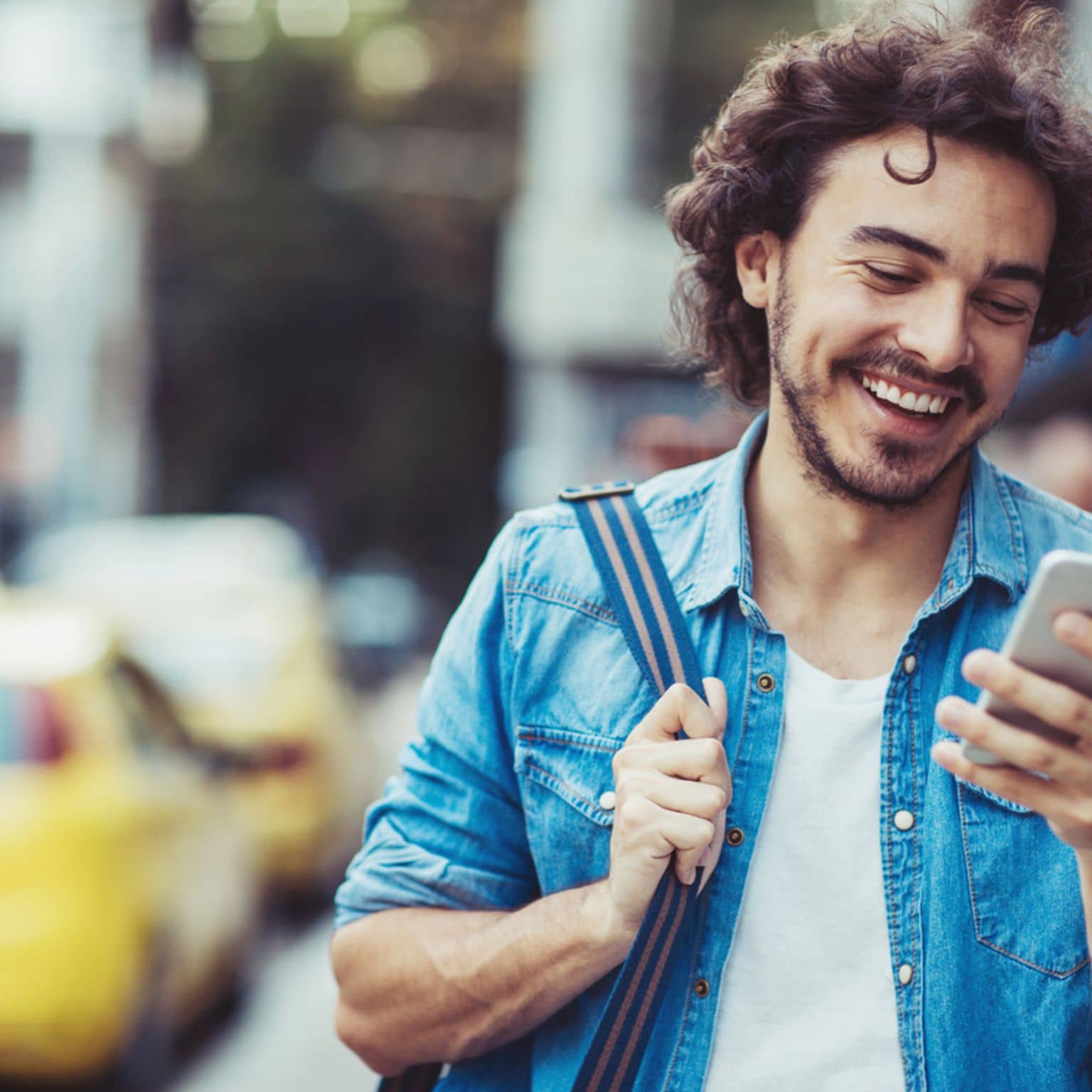 Bild: Junger Mann mit Tasche auf der Schulter schaut auf sein Handy.