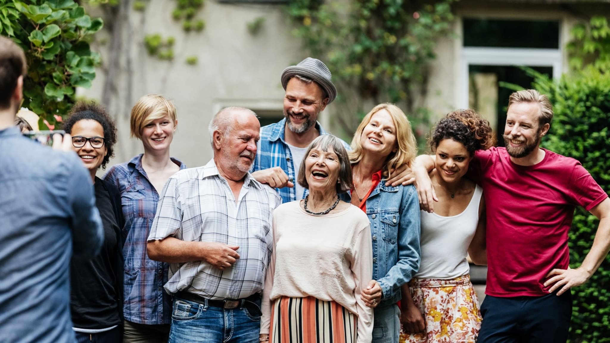 DAK Wahltarife: Ein Mann macht ein Foto von seinen Freunden und seiner Familie in einem grünen Hinterhof.