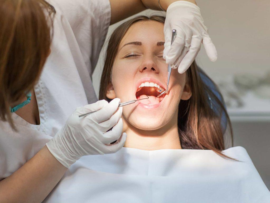 Bild: Eine Zahnarzthelferin kontrolliert die Zähne bei einer jungen Frau.