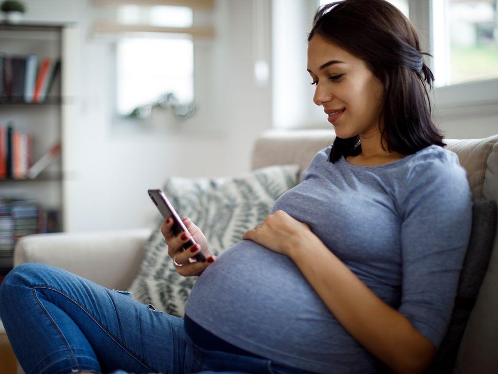 Bild: Lächelnde schwangere Frau mit Handy zu Hause.