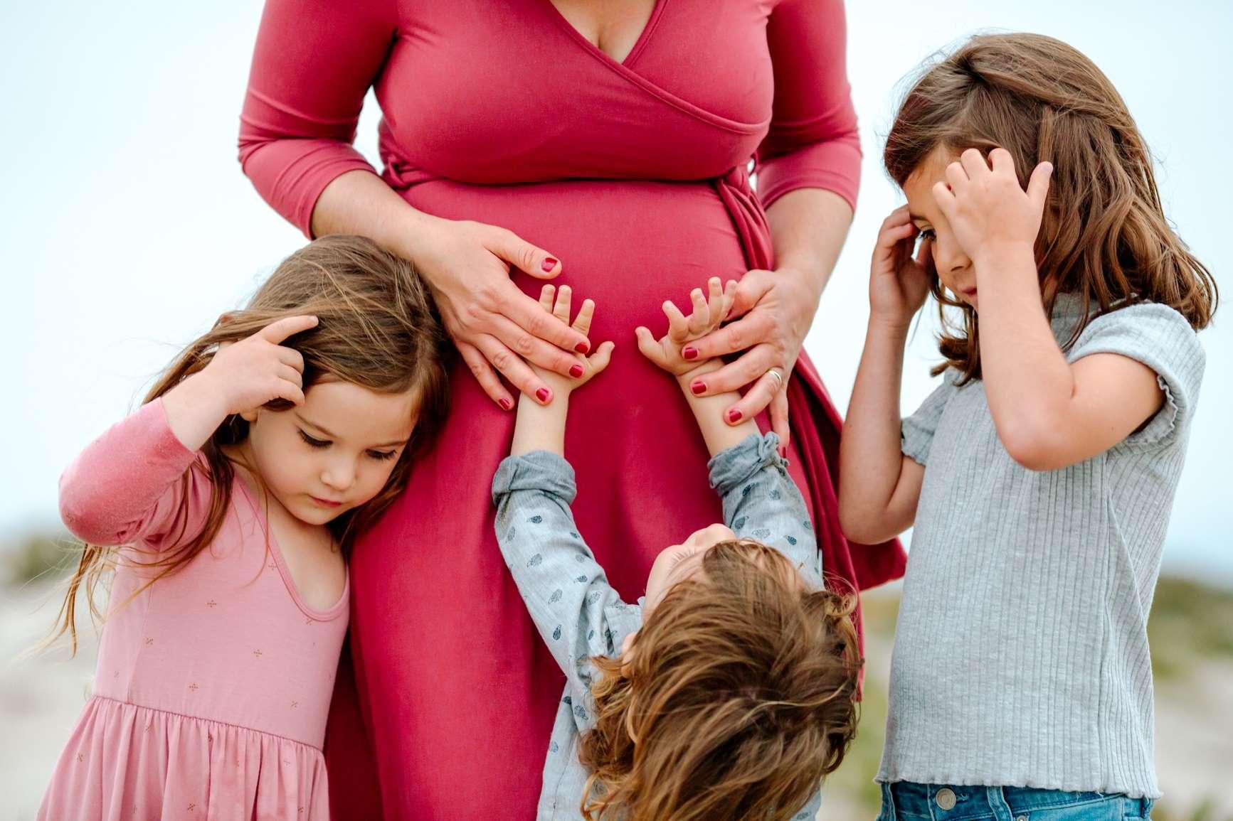 Hebammensuche: Kinder umarmen Bauch einer Schwangeren.