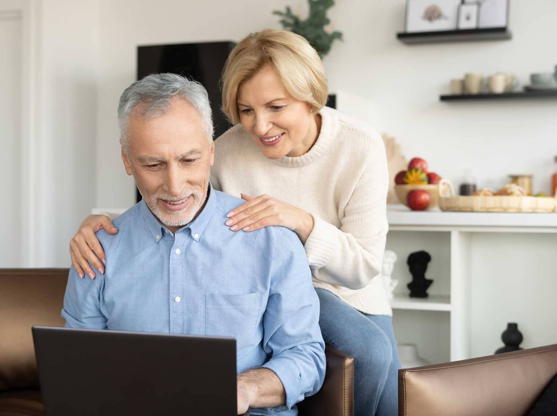 Älteres Paar sitzt auf dem Sofa und schaut gemeinsam auf den Bildschirm eines Notebooks.