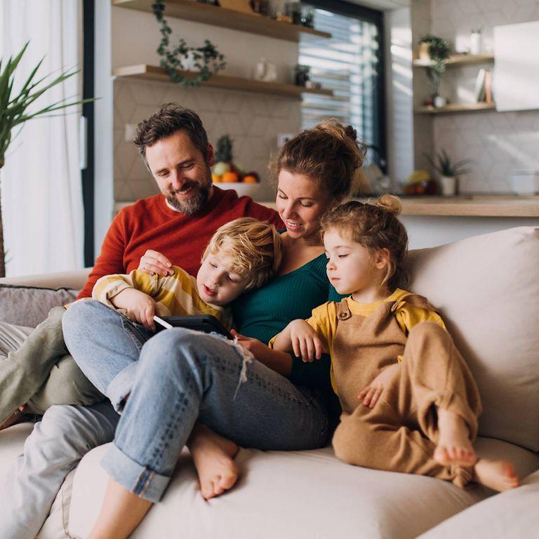 Vorteile bei der DAK: Familie sitzt entspannt auf dem Sofa und guckt in ein Buch