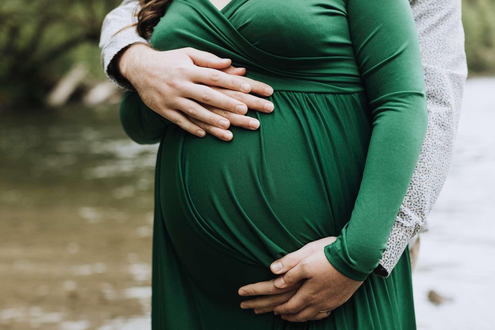 Hebammenliste: Mann umarmt Bauch einer Schwangeren von hinten.