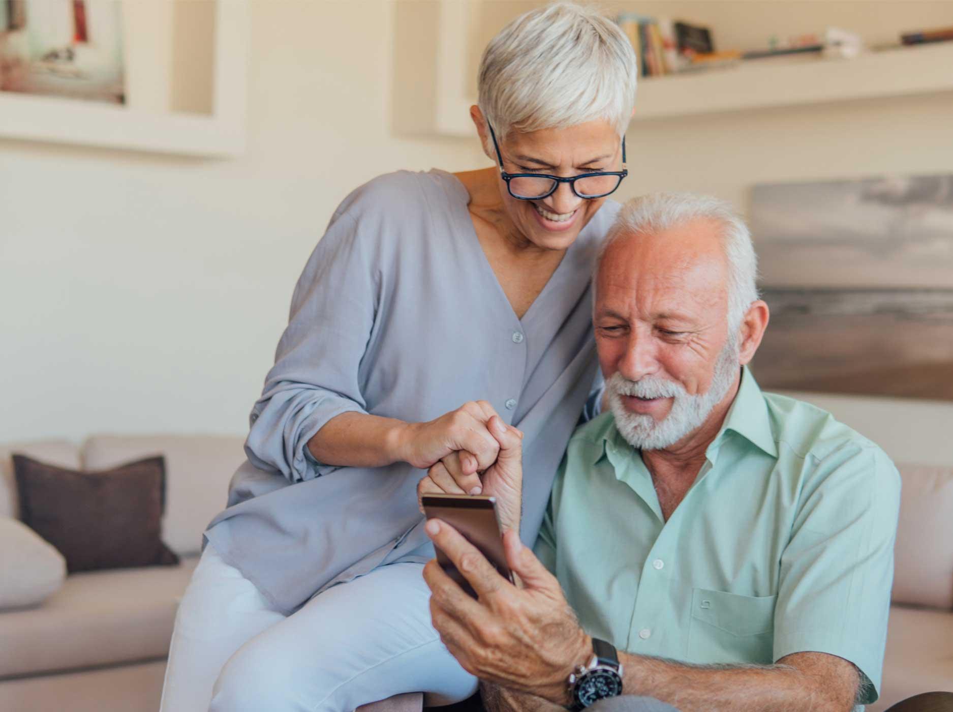 Herzschwäche: Älteres Paar sitzt gemeinsam auf einem Sessel und schaut auf ein Handy.