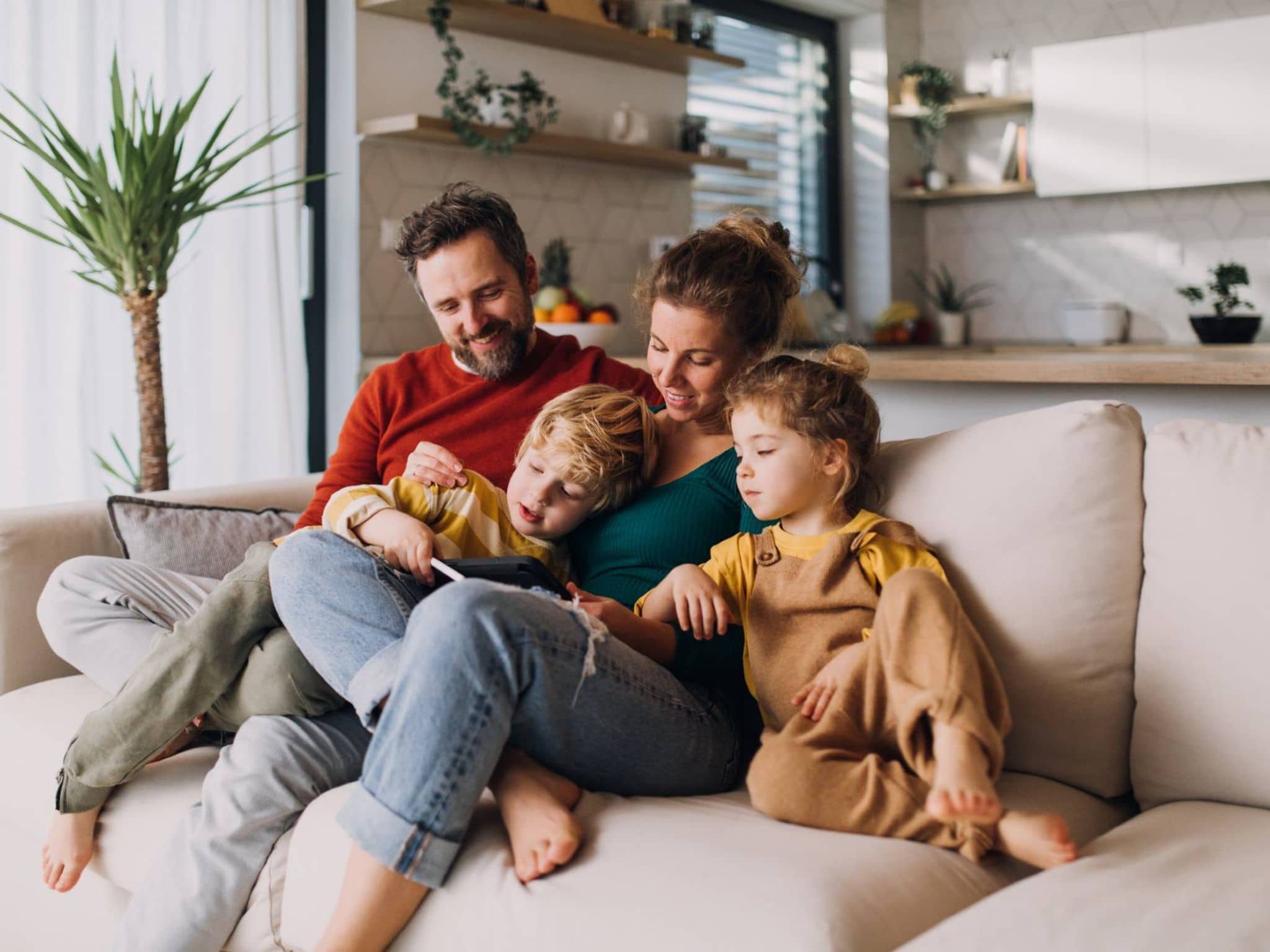 Online-Seminare für Familien: Mutter, Vater und zwei Kinder sitzen auf der Couch und lesen gemeinsam