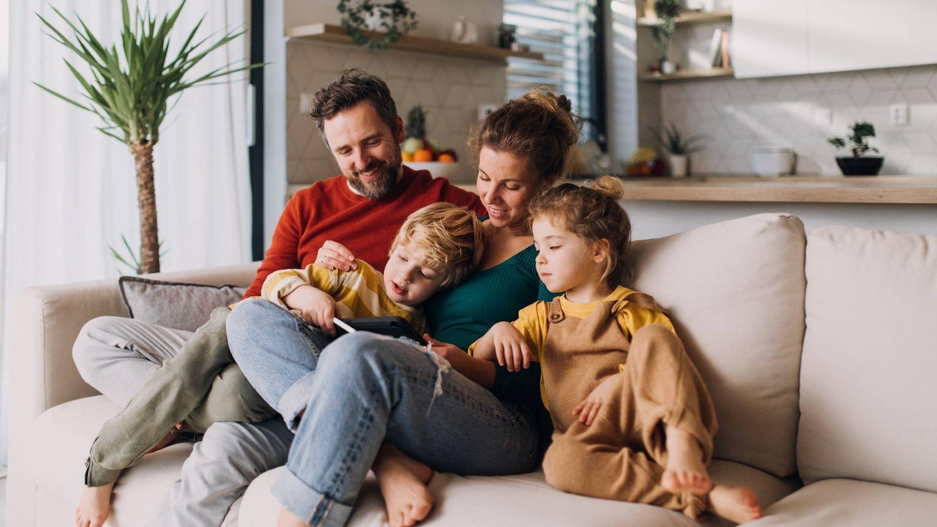 Online-Seminare für Familien: Mutter, Vater und zwei Kinder sitzen auf der Couch und lesen gemeinsam