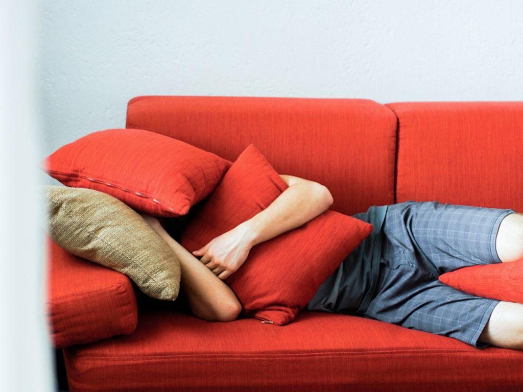 Stress abbauen: Mann liegt auf roter Couch und vergräbt sich in Kissen