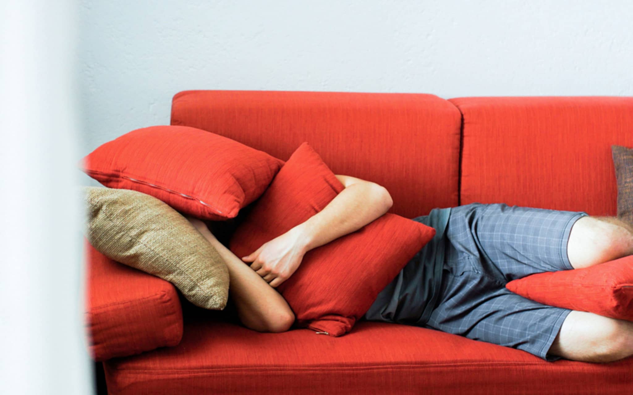 Stress abbauen: Mann liegt auf roter Couch und vergräbt sich in Kissen