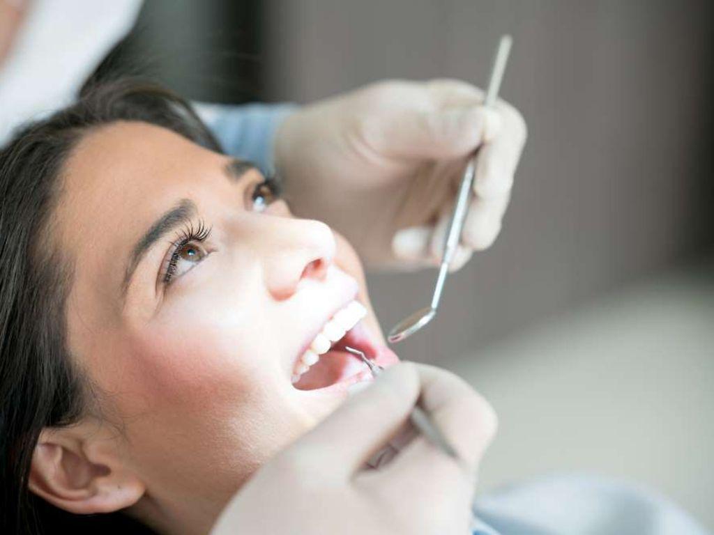 Zahnvorsorge: Junge Frau sitzt mit geöffnetem Mund beim Zahnarzt und wird untersucht.