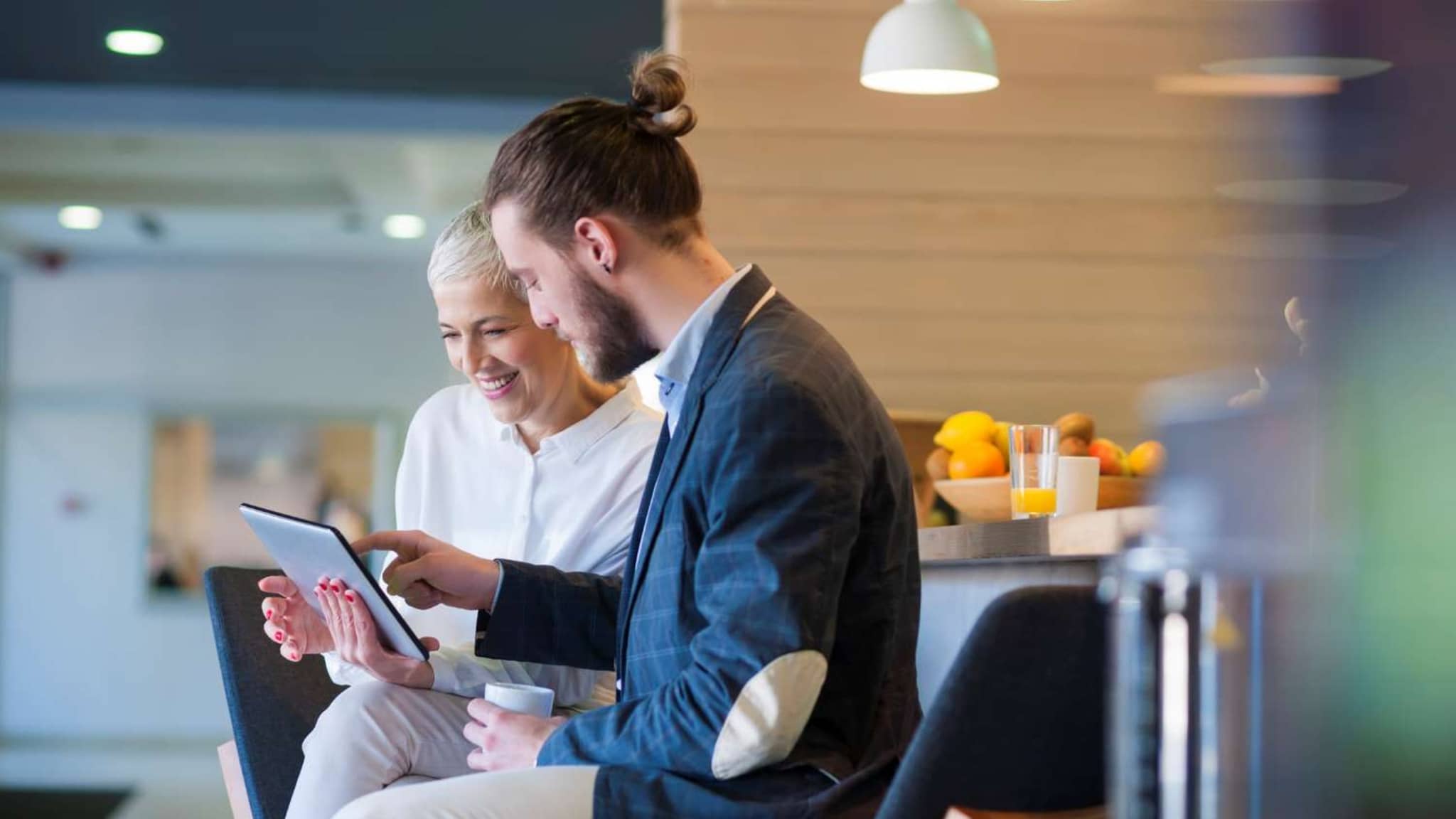 Patientenschulung Ernährung: Ältere Frau und junger Mann nutzen digitales Tablet in einem Seminarraum.