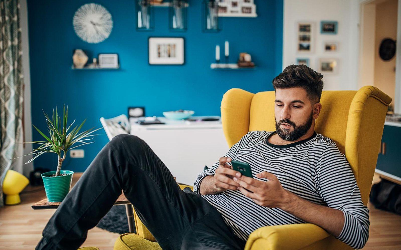 DAK App: Mann sitzt auf Sessel und nutzt entspannt sein Smartphone