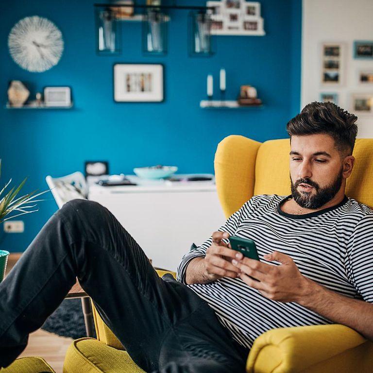 DAK App: Mann sitzt auf Sessel und nutzt entspannt sein Smartphone