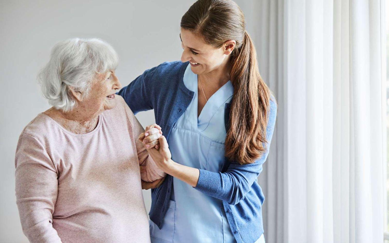 Pflege in Pflegeheimen: Pflegerin unterstützt ältere Frau beim Gehen.