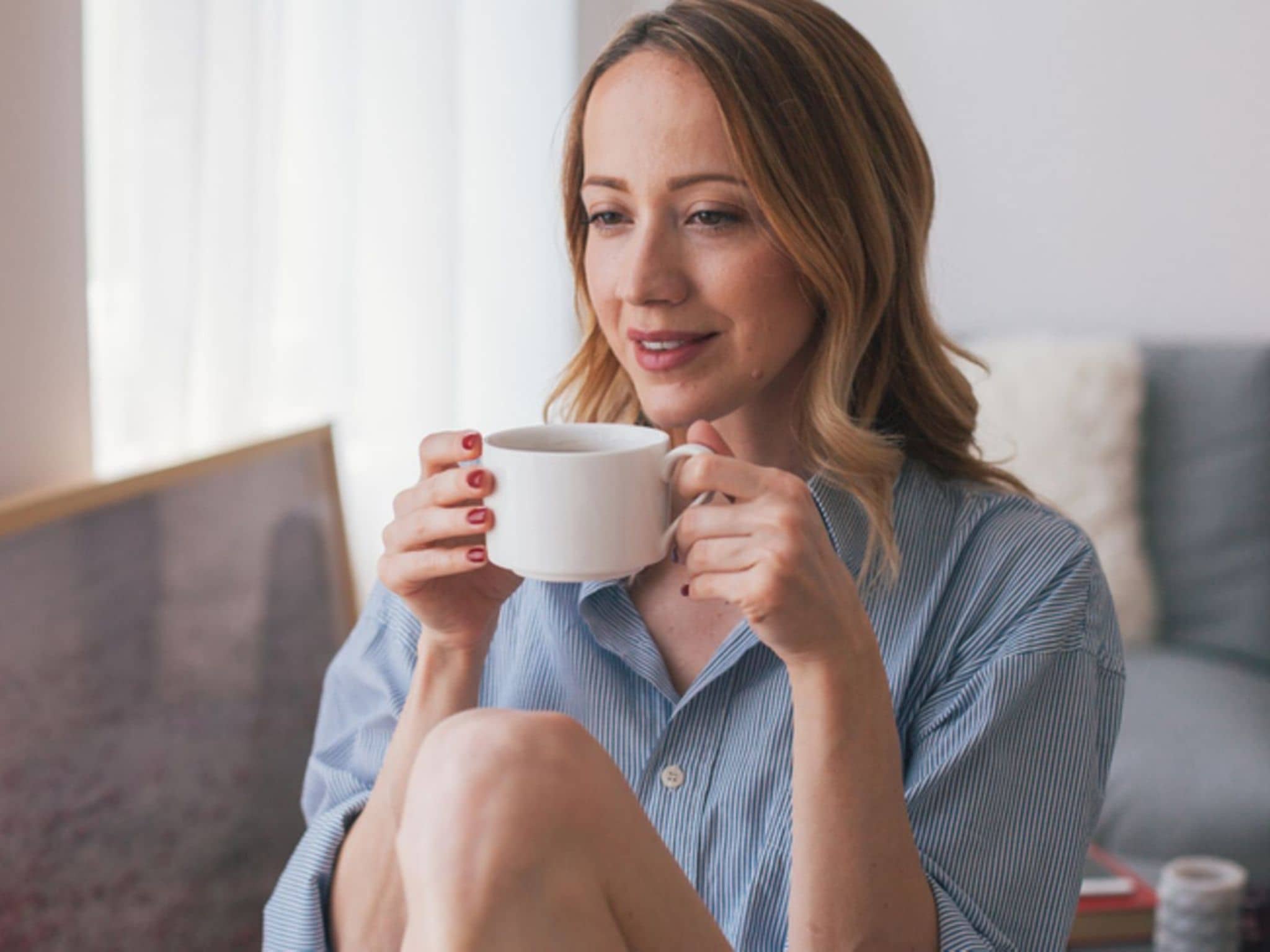 Eine Frau sitzt am Tisch und hält genüsslich eine Tasse in der Hand