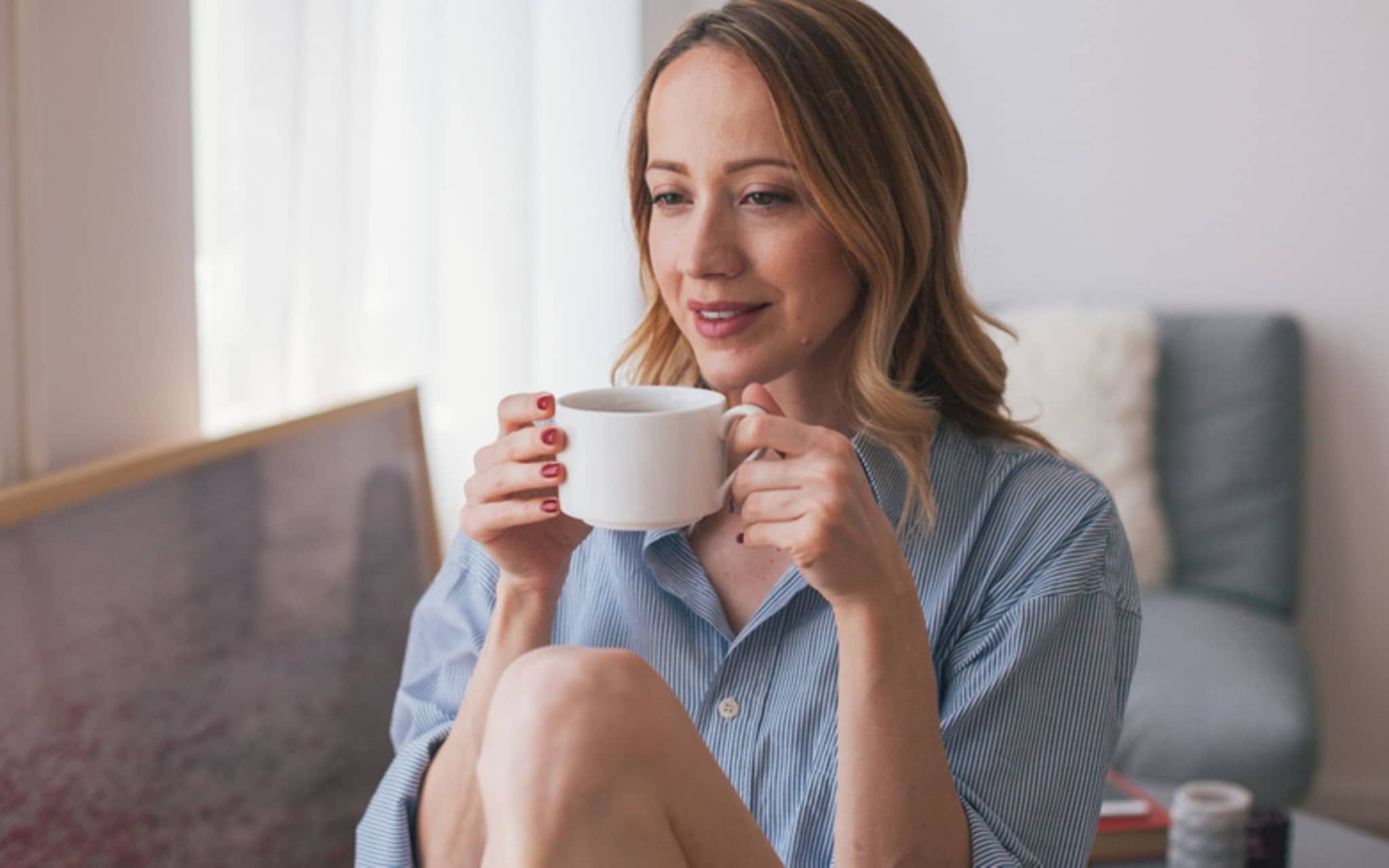 Eine Frau sitzt am Tisch und hält genüsslich eine Tasse in der Hand