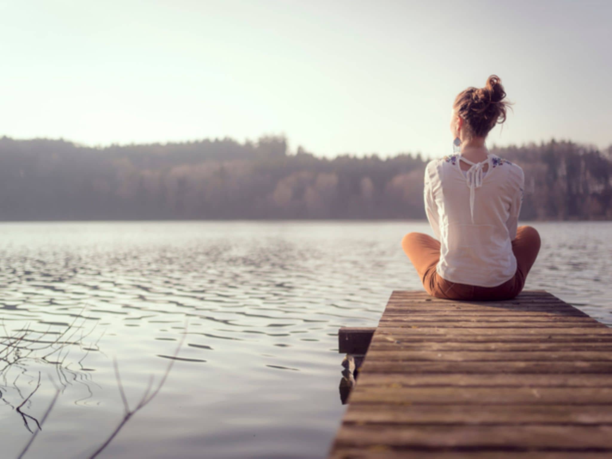 Frau sitzt an einem See auf Steg