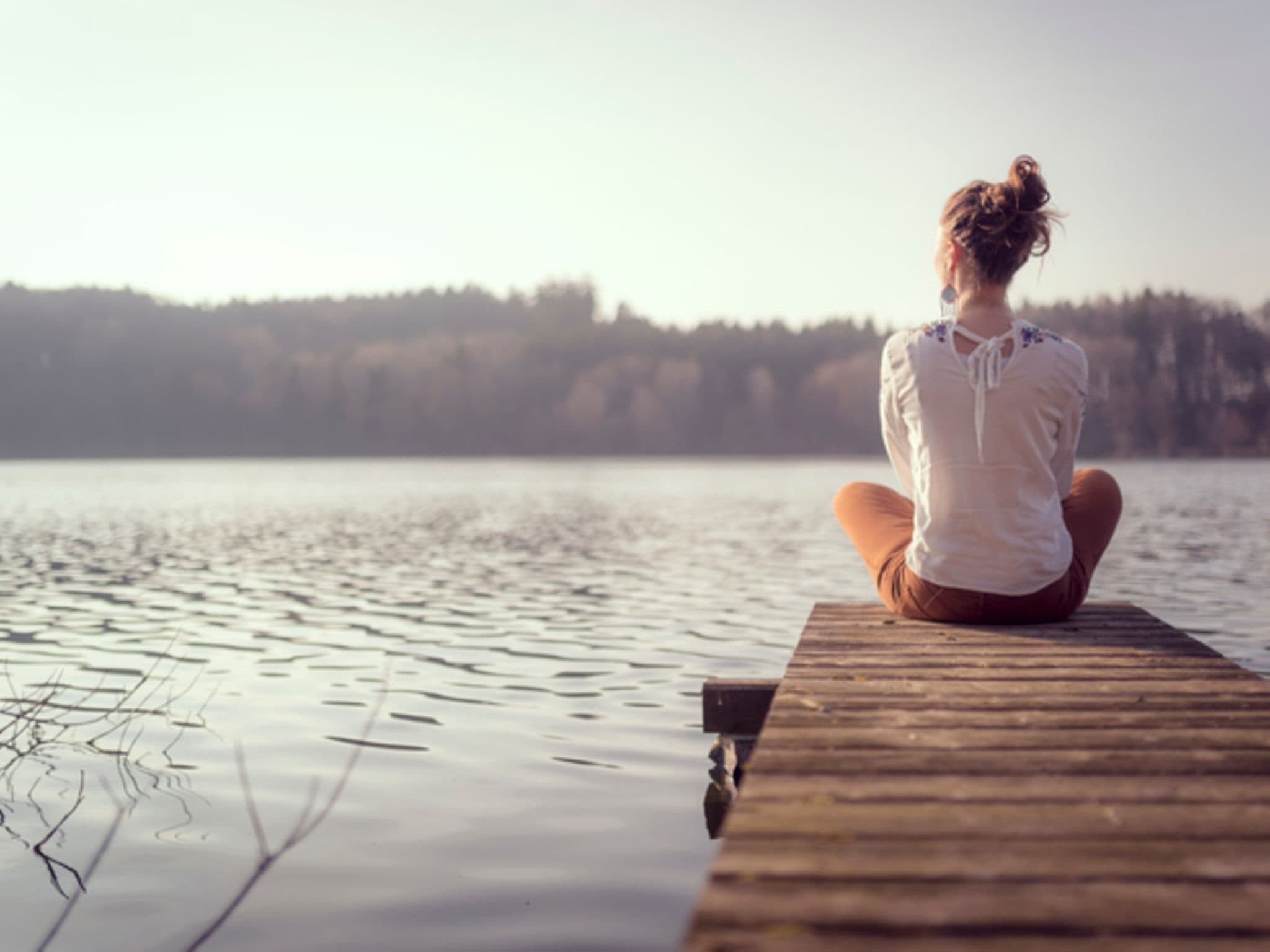 Frau sitzt an einem See auf Steg