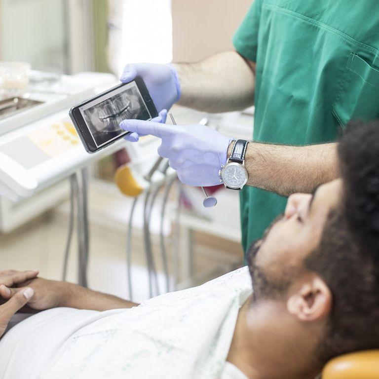 Symbolfoto elektronische Patientenakte: Mann sitzt auf Zahnarztstuhl und schaut auf Röntgenbild auf einem Handy.