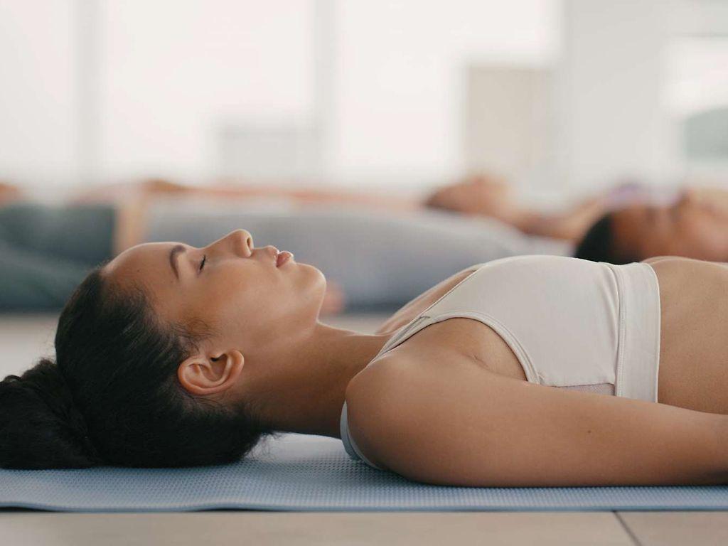 Progressive Muskelentspannung: Junge Frau liegt entspannt auf einer Yogamatte.