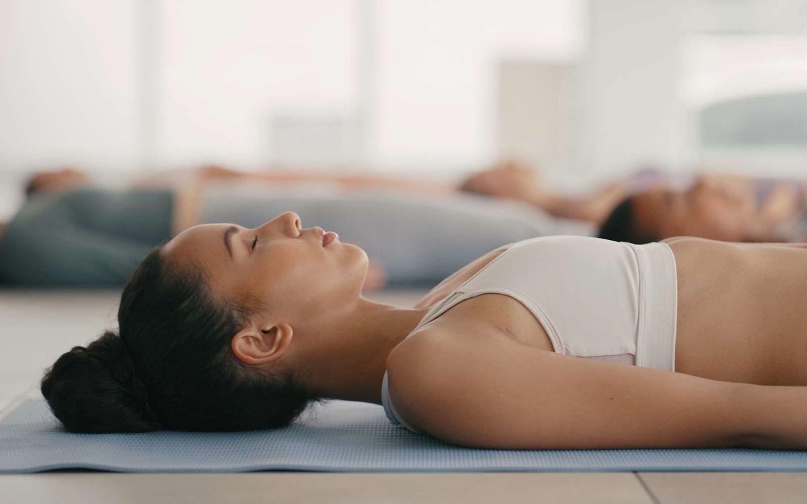 Progressive Muskelentspannung: Junge Frau liegt entspannt auf einer Yogamatte.
