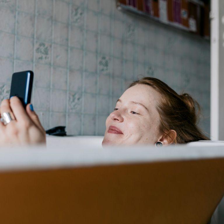 Frau liegt mit Smartphone in der Badewanne