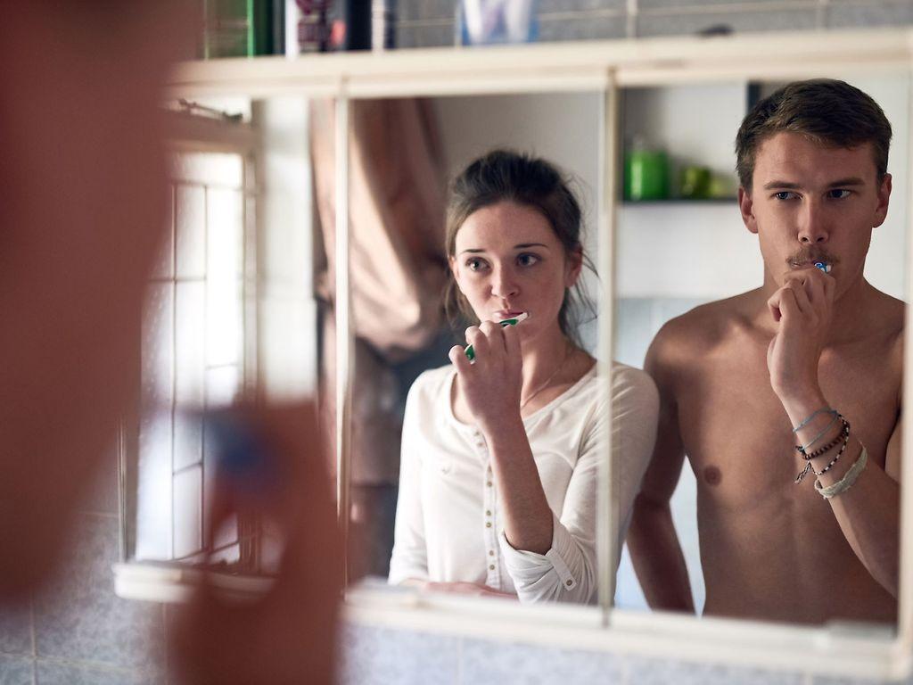 Professionelle Zahnreinigung: Paar putzt gemeinsam vor dem Spiegel Zähne.