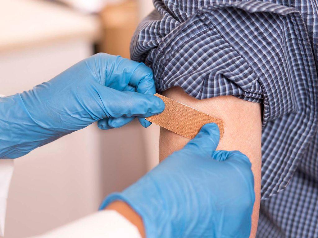 Bild: Eine Arzthelferin klebt ein Pflaster auf einen Arm, der gerade eine Impfung erhalten hat.