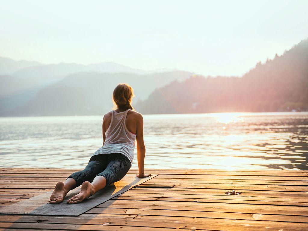 Bild: Frau liegt auf der Matte und macht Yoga auf einem Steg am See