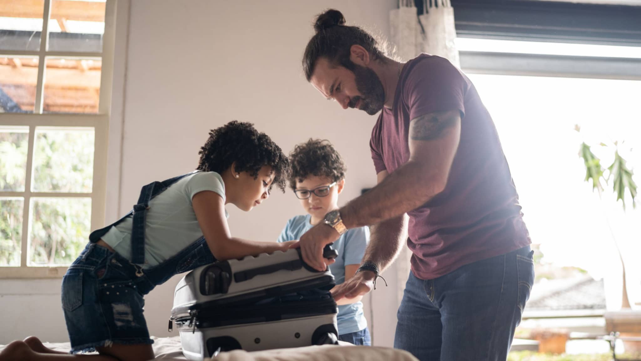 Reisen und Freizeit: Junger Vater packt mit seinen beiden Kindern einen Koffer.