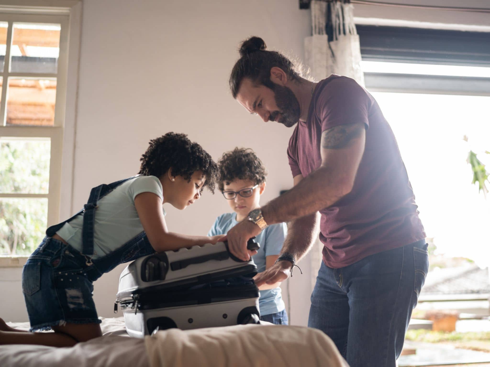 Reisen und Freizeit: Junger Vater packt mit seinen beiden Kindern einen Koffer.