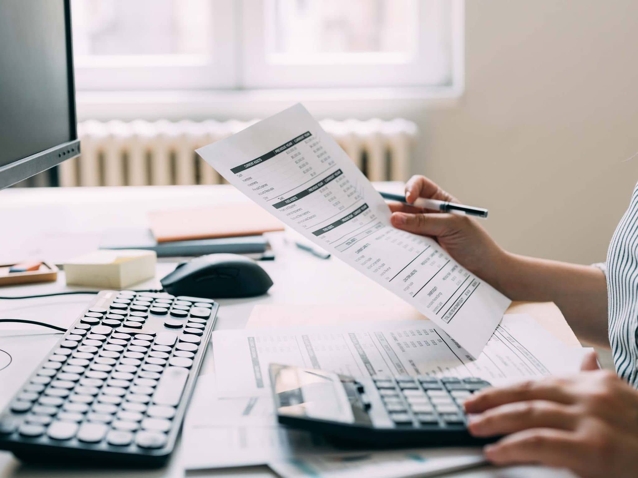 Symbolfoto Abrechnungsbetrug: Frau am PC mit Rechnungen in der Hand.