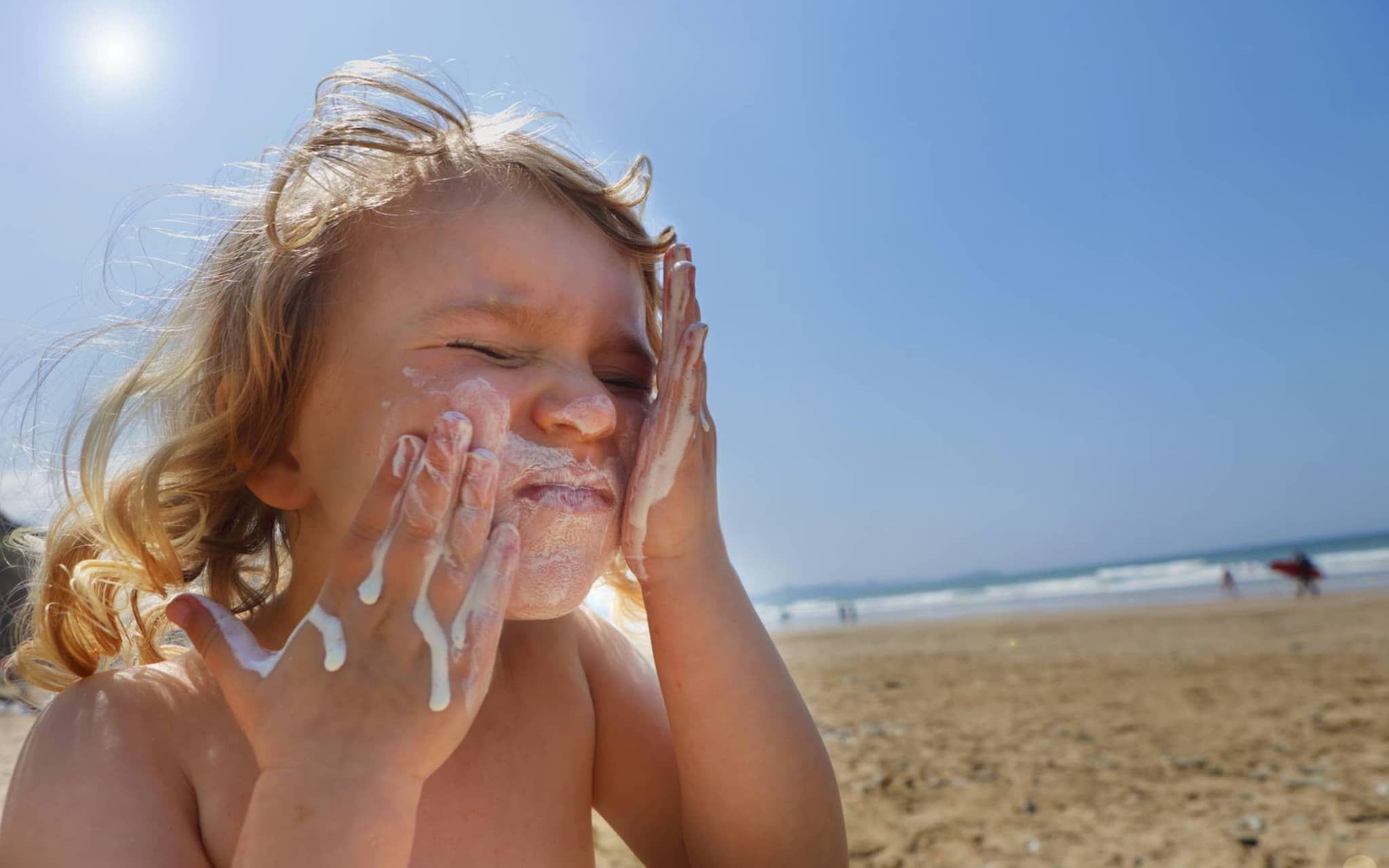 Sonnenbrand bei Kindern: Kleines Mädchen cremt sich am Strand das Gesicht ein